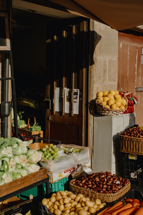 Produce market stall displaying fresh vegetables and fruits in woven baskets outside a storefront.