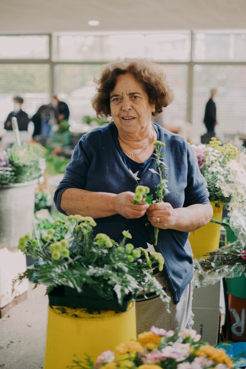 Woman arranging fresh flowers and plants in a greenhouse or market setting in Guimarães.