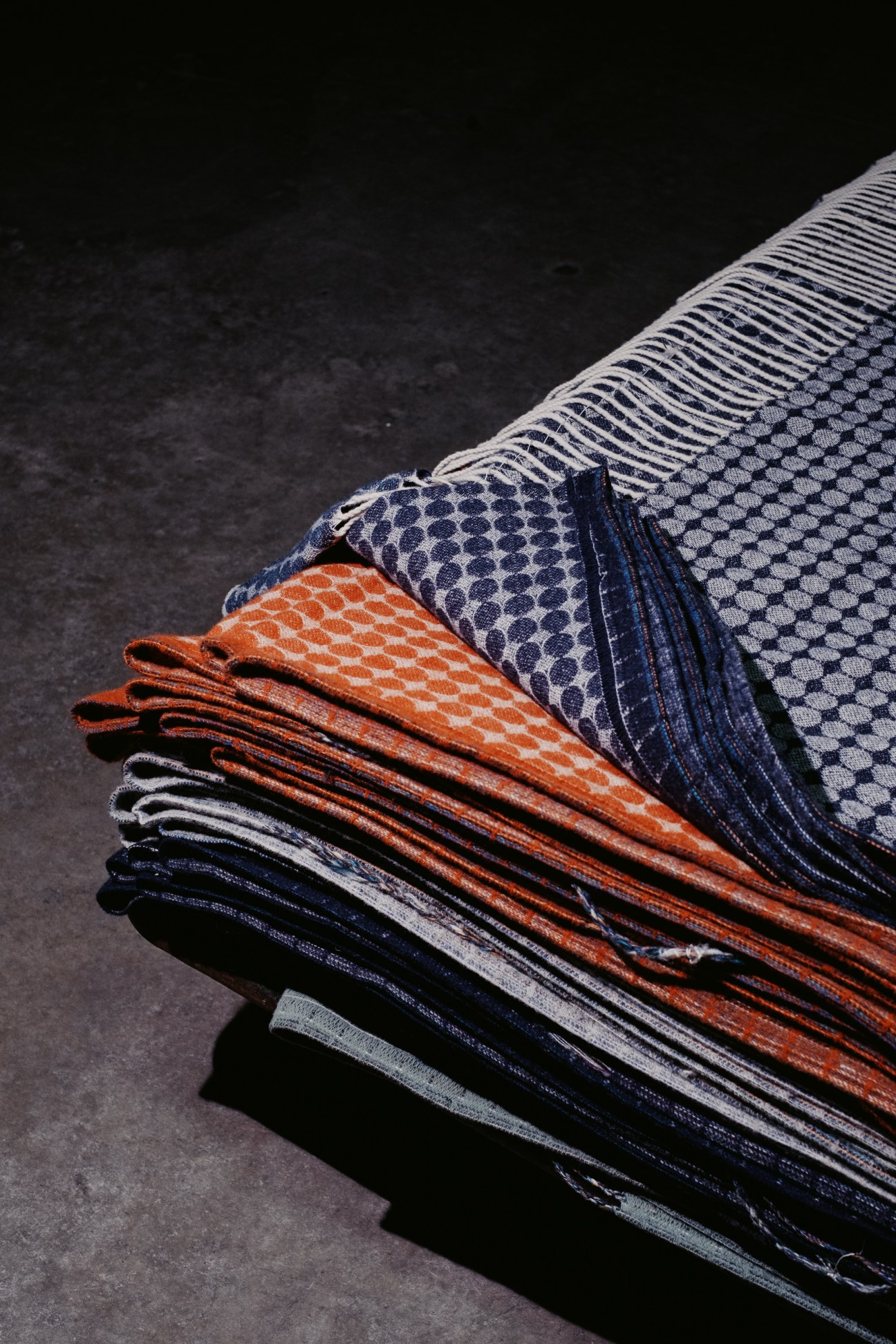 Stack of folded textiles with geometric patterns in orange, blue and white colors on dark surface