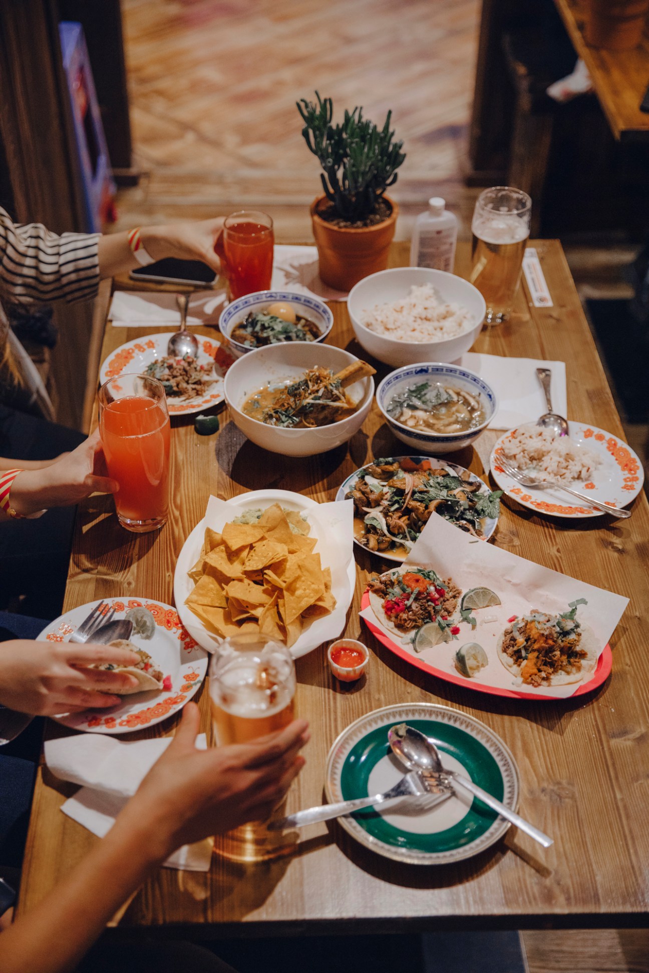 Overhead view of a wooden table with various dishes, tacos, drinks, and tortilla chips at Markthalle Pfefferberg