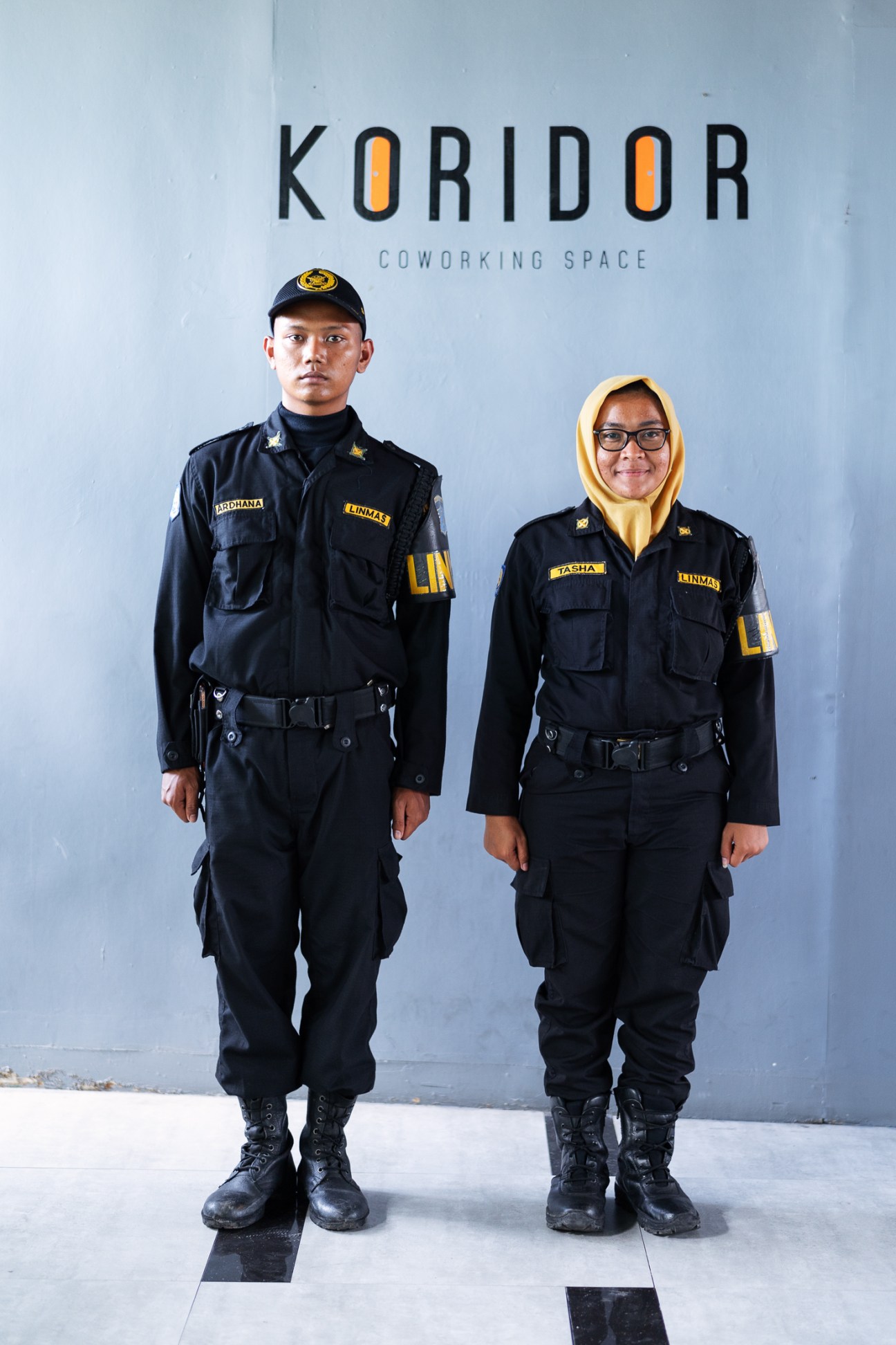 Two security guards in black uniforms standing in front of Koridor Coworking Space wall