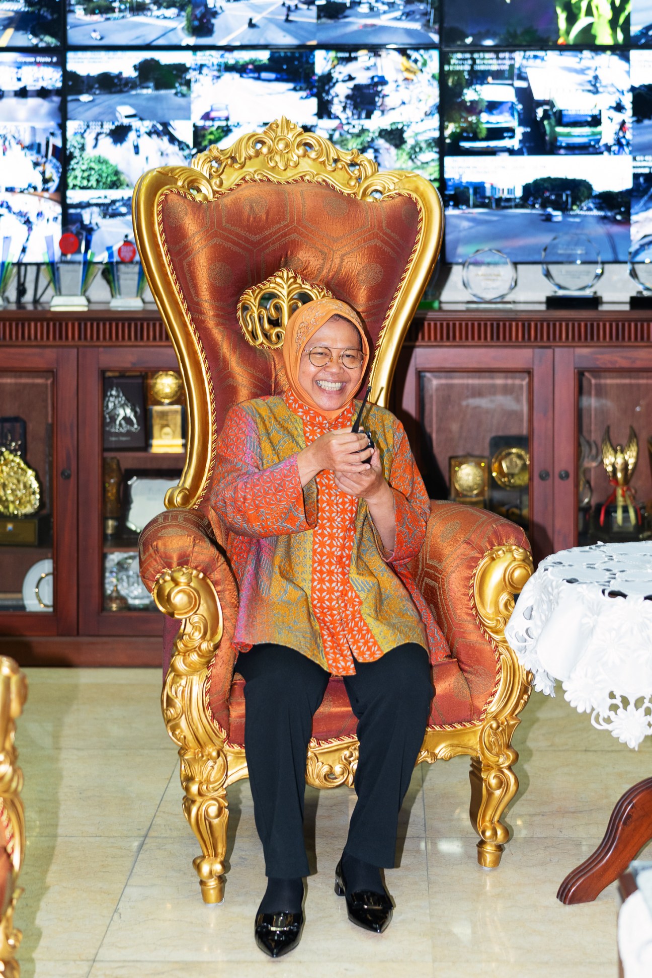 Woman in orange headscarf and patterned clothing sitting in ornate golden throne-like chair in control room