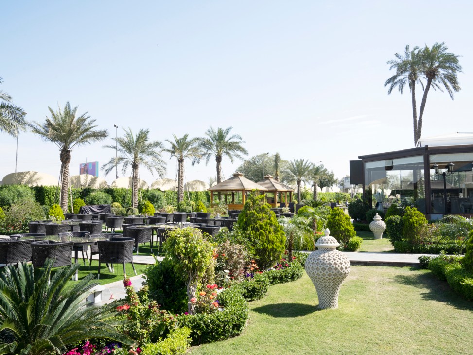 Outdoor dining terrace with dark wicker furniture surrounded by lush landscaping, palm trees and decorative planters