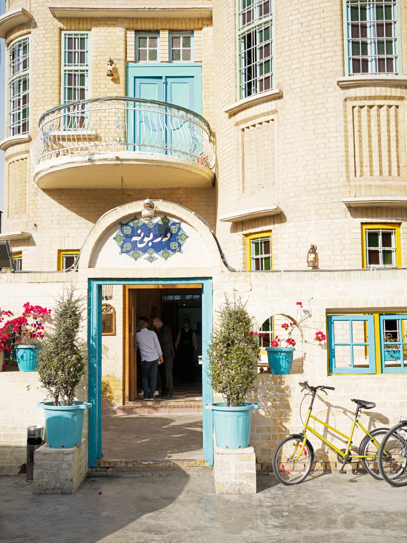 Exterior of Darbunah restaurant showing cream-colored building with turquoise doors, decorative balcony, and yellow bicycle