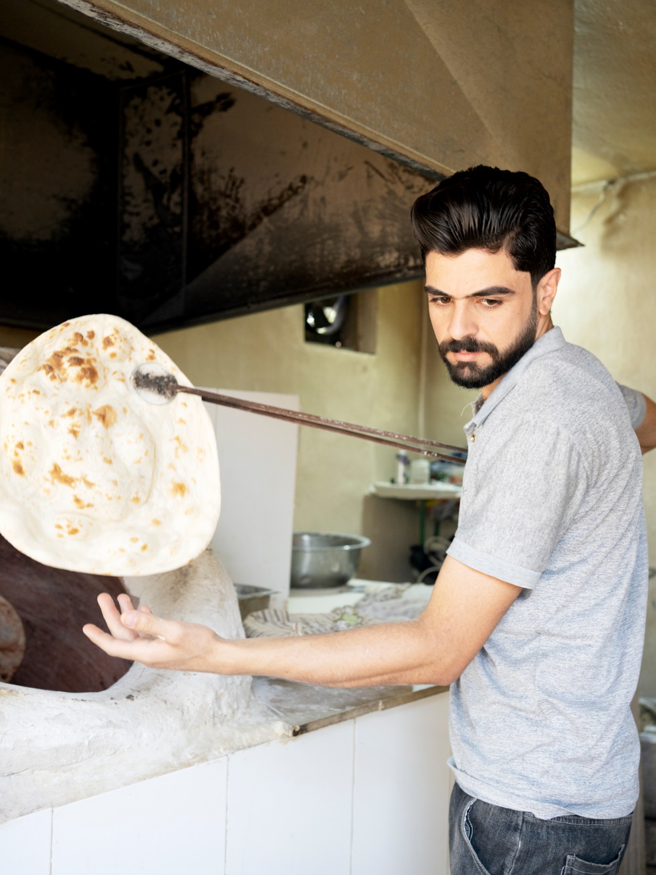 Man in grey shirt tossing flatbread dough in a restaurant kitchen