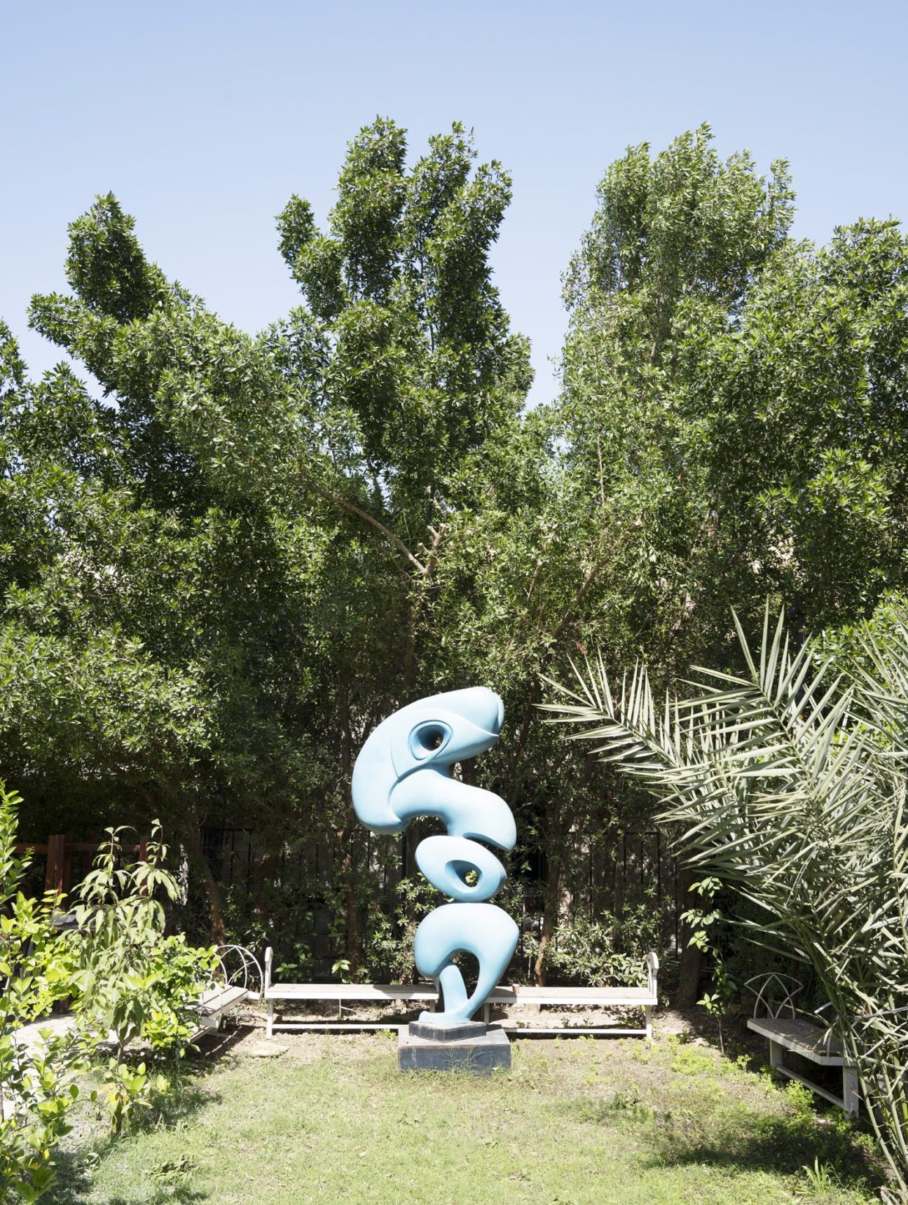White sculptural artwork displayed in garden setting with palm trees and lush vegetation