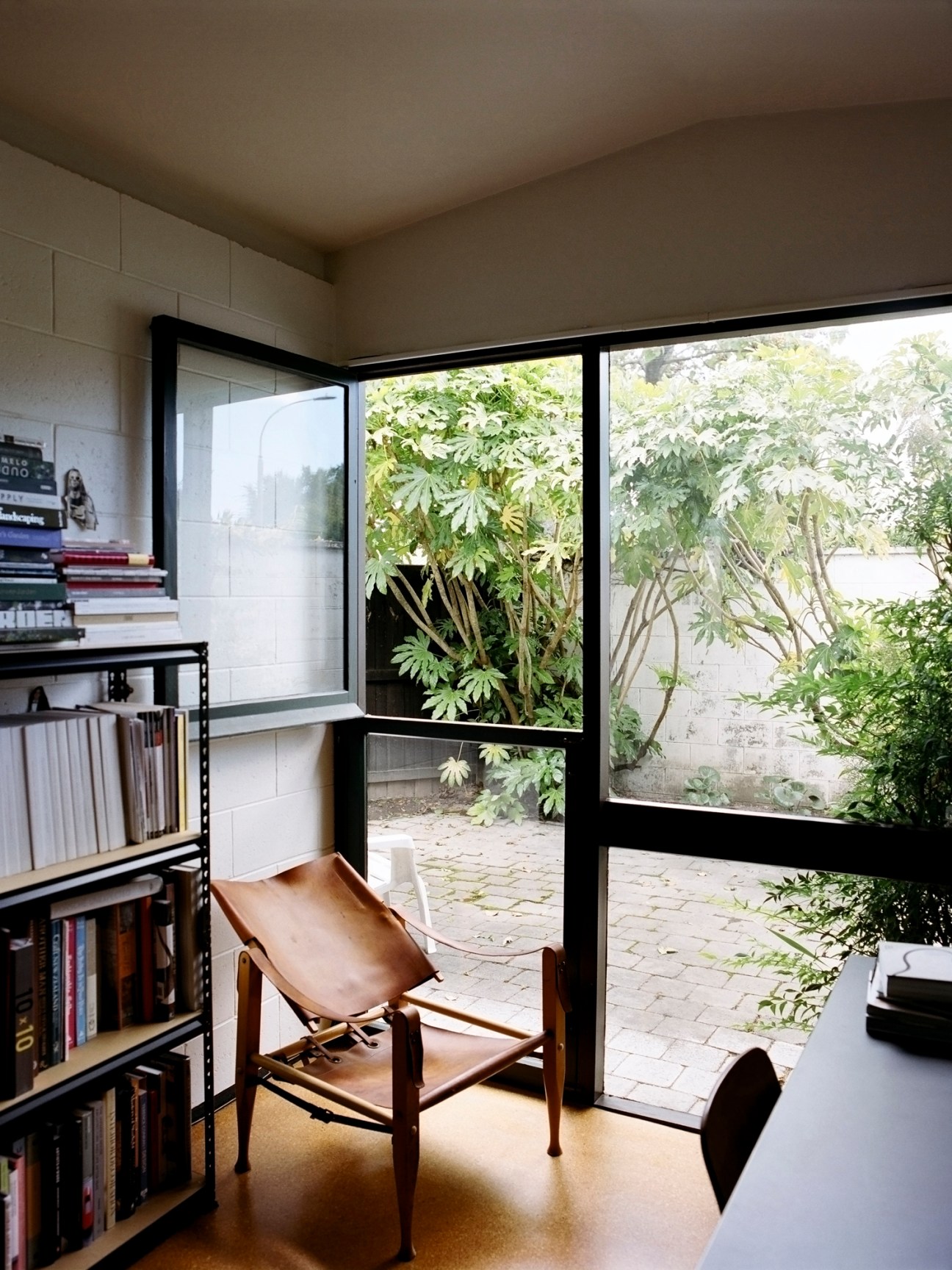 Kaare Klint Safari Chair beside bookshelf and large window overlooking garden courtyard