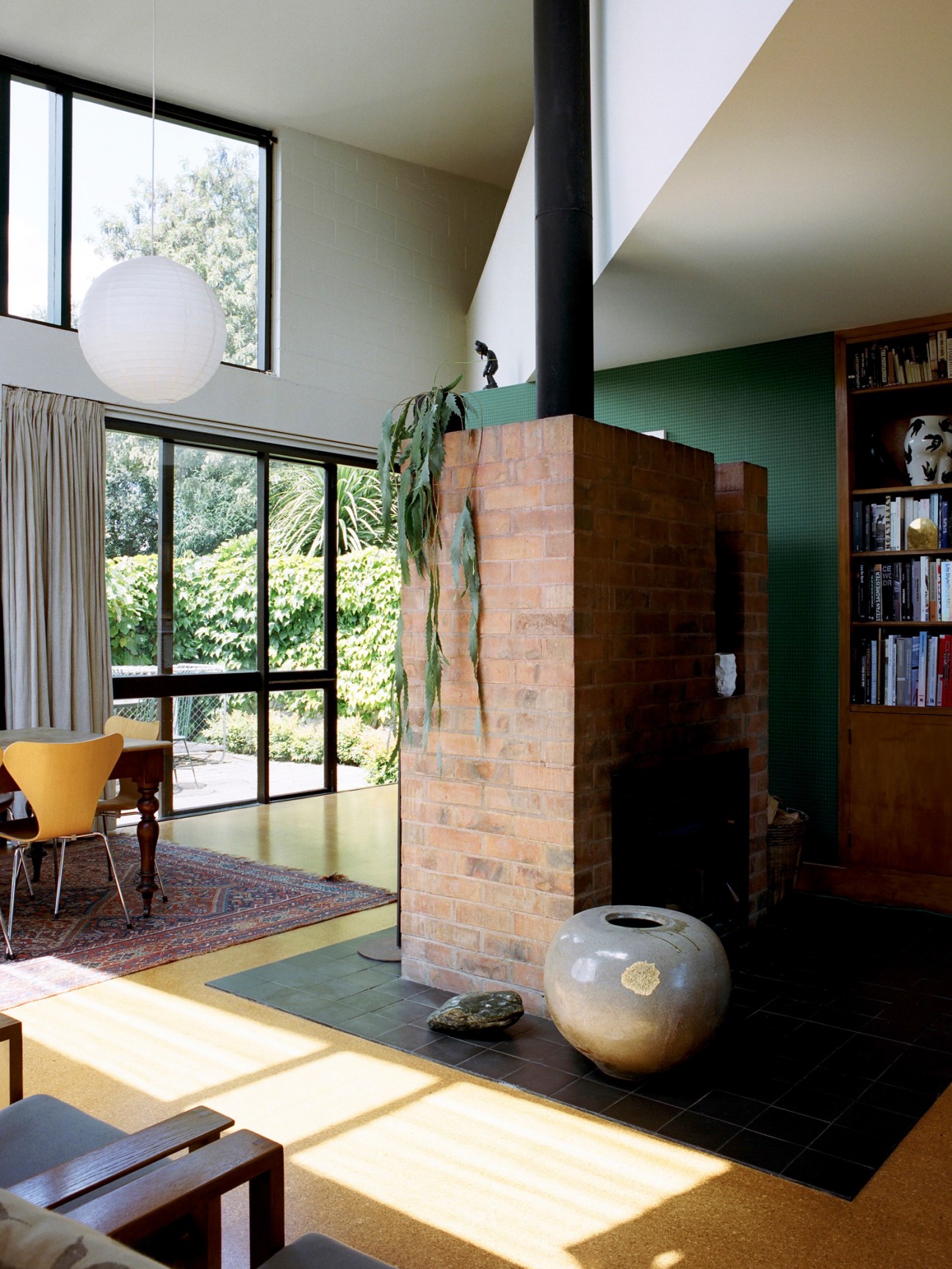 Modern living room with brick fireplace, mezzanine level, and floor-to-ceiling windows overlooking garden