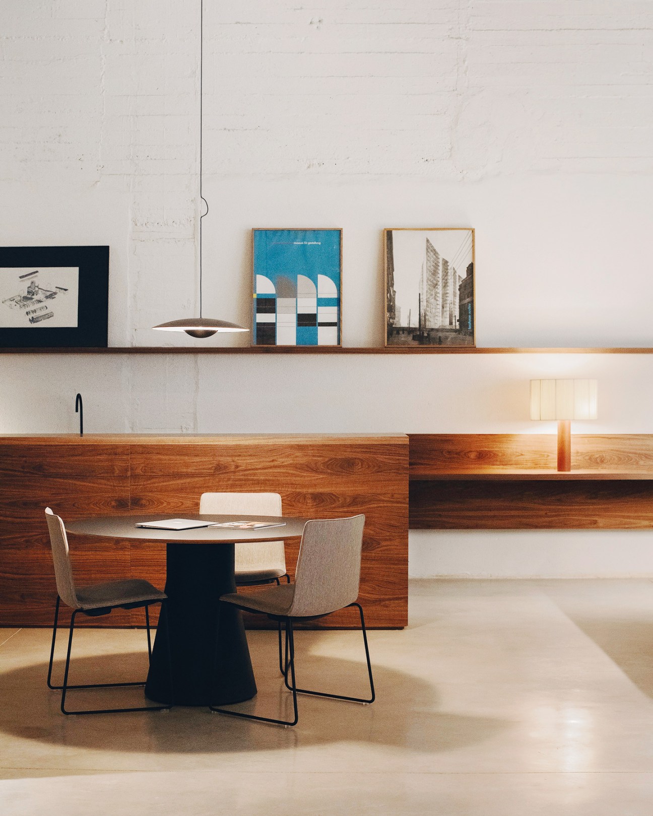 Minimalist office interior with wooden desk, modern chairs, white walls, and framed artwork on shelves.