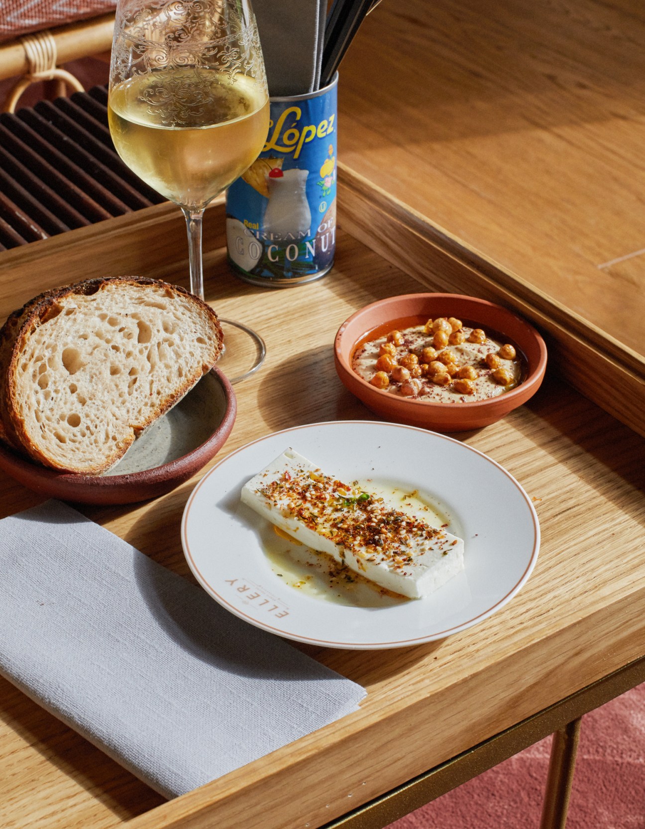 White cheese with spices, bread, nuts in terracotta bowl, and white wine on wooden serving tray