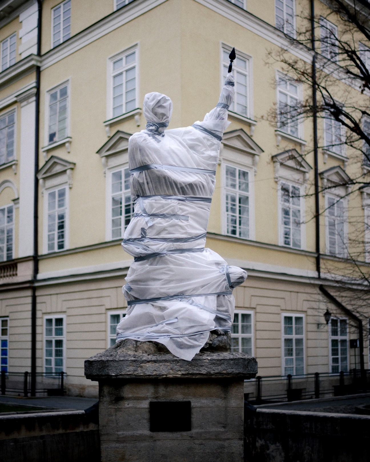 Statue wrapped in white protective material and tape in central Lviv square