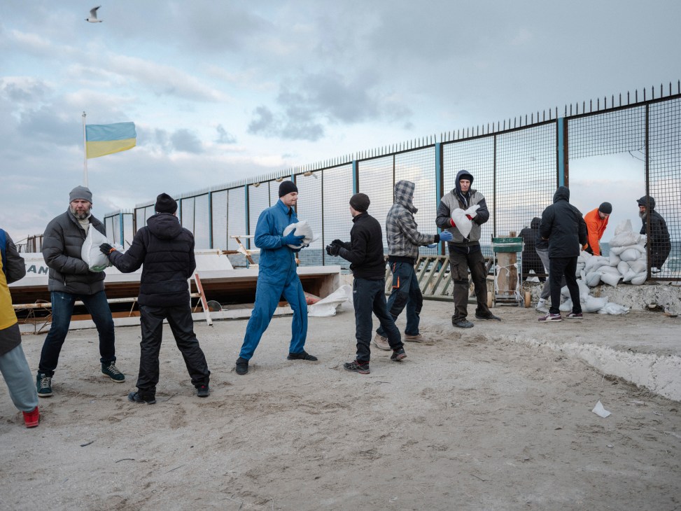 Group of civilians working together on a beach in Odesa loading sandbags onto a truck for defensive purposes