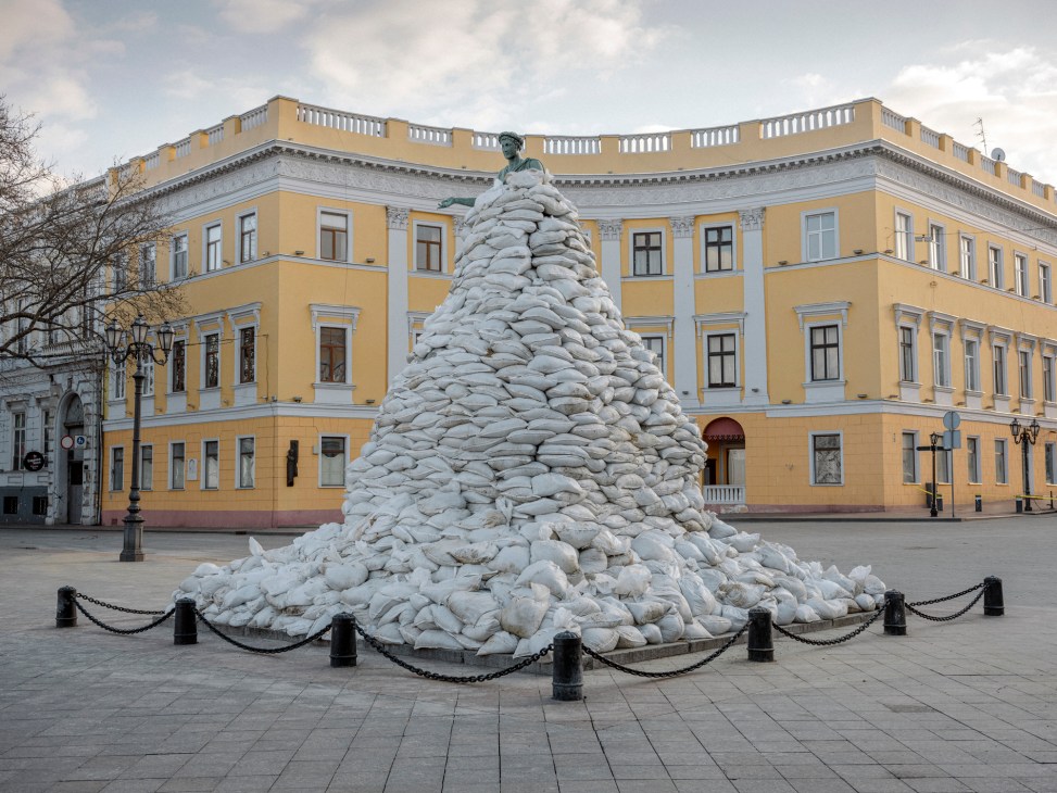 Large mound of sandbags protecting monument to Duc de Richelieu in Odesa with yellow palace building behind