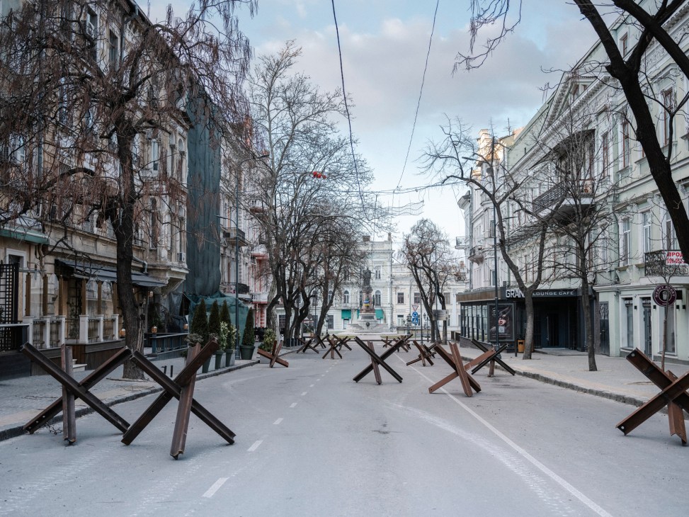 Anti-tank hedgehogs blocking a snow-covered street in Odesa with historic buildings and bare winter trees