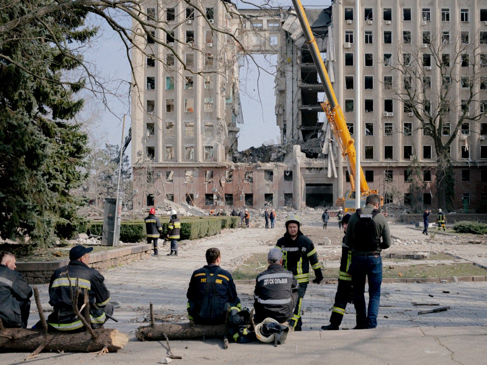 Heavily damaged multi-story administrative building in Mykolaiv with emergency workers and crane in foreground