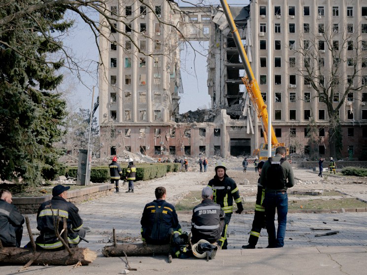 Heavily damaged multi-story administrative building in Mykolaiv with emergency workers and crane in foreground