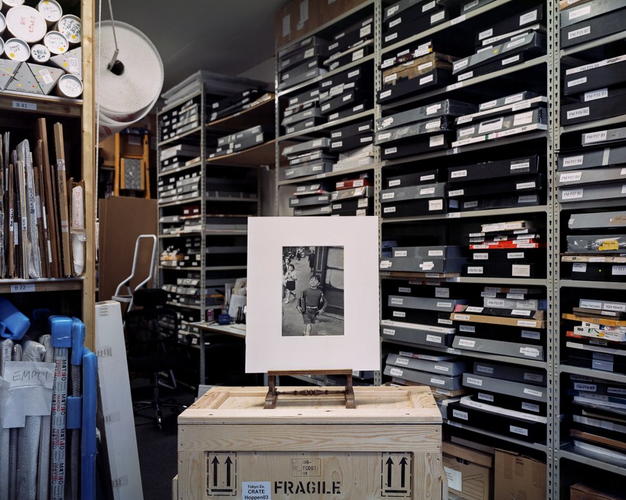 Black and white photograph displayed on easel in archival storage room with labeled film canisters on shelves