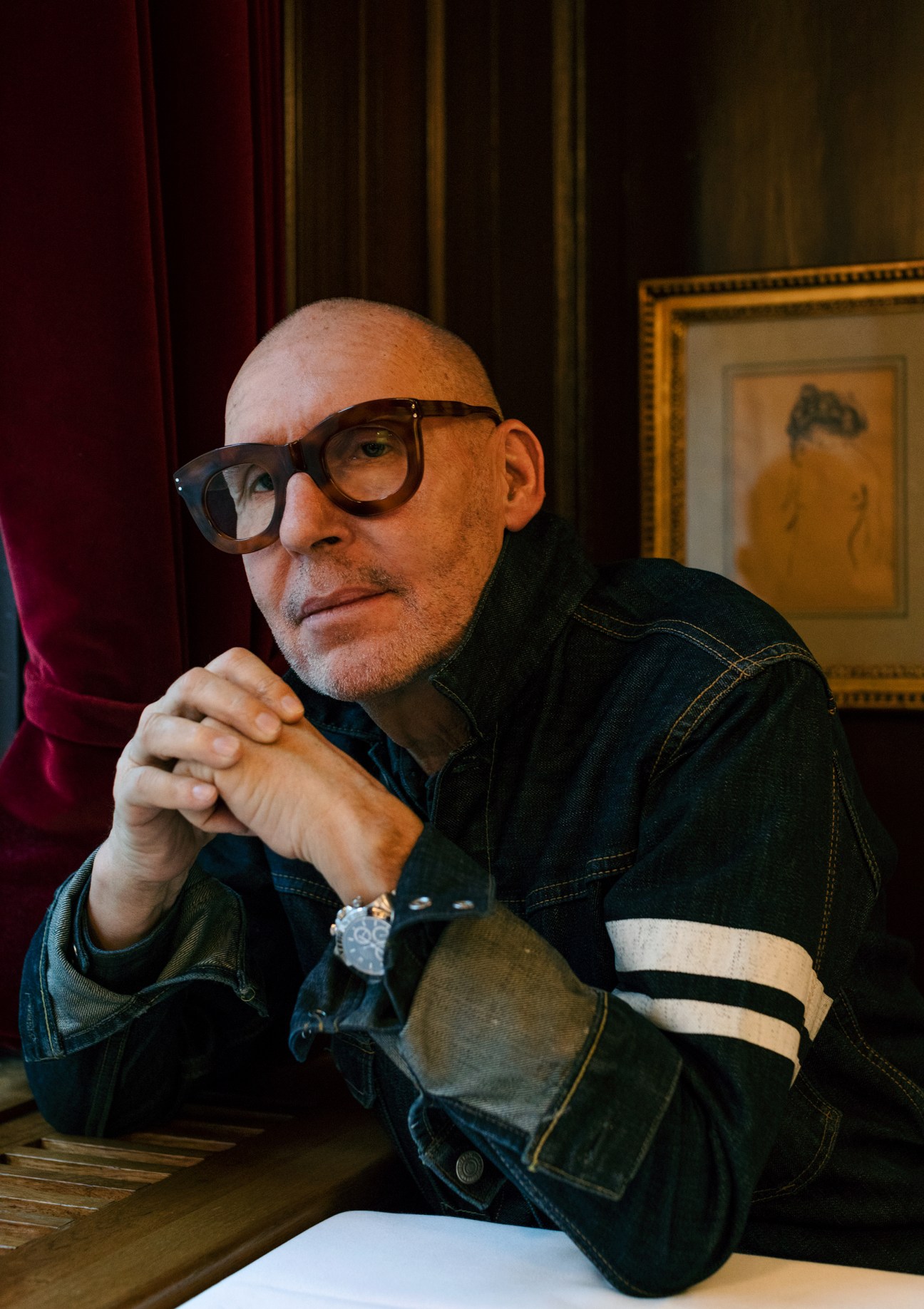 Michel Comte sits at a table in Kronenhalle restaurant wearing glasses and a denim jacket