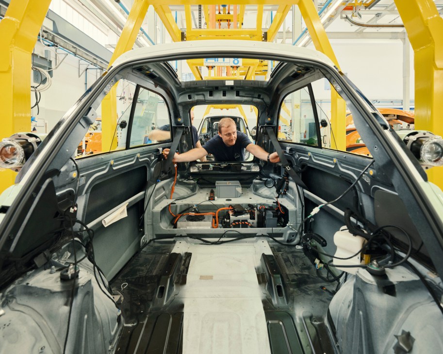 A worker installing components inside the metal frame of a Microlino electric car during factory assembly