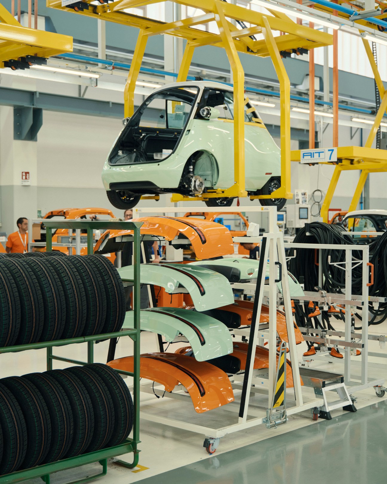 Interior of Microlino factory showing production line with suspended green car body and stacked components