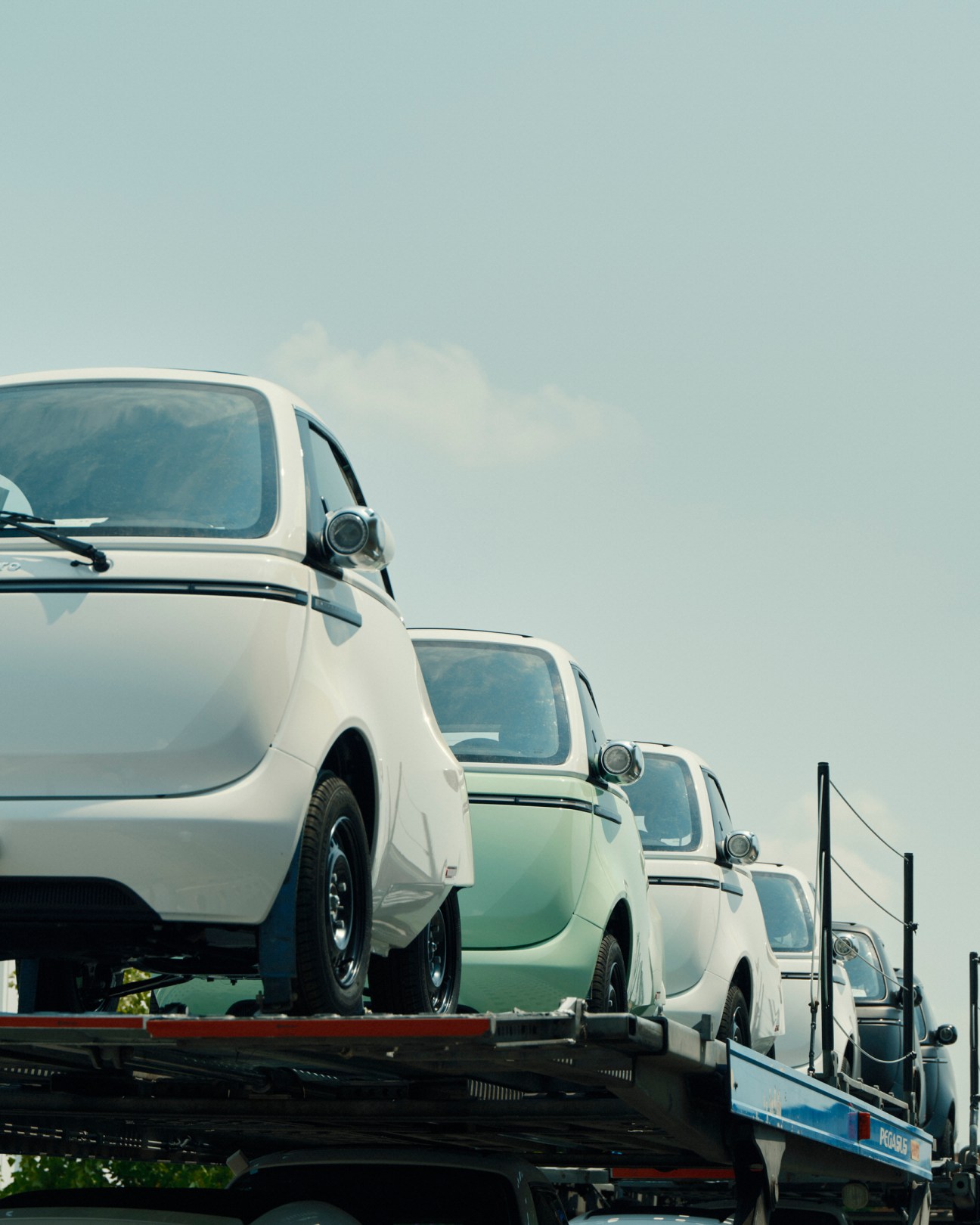 White Microlino electric cars lined up on a car carrier truck ready for delivery