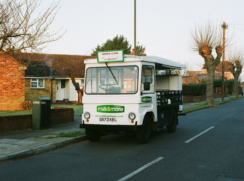 White Milk & More delivery truck parked on residential street next to brick houses