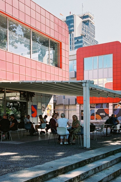 People dining at outdoor tables under a covered terrace at the modern red-tiled MKC cultural centre in Skopje