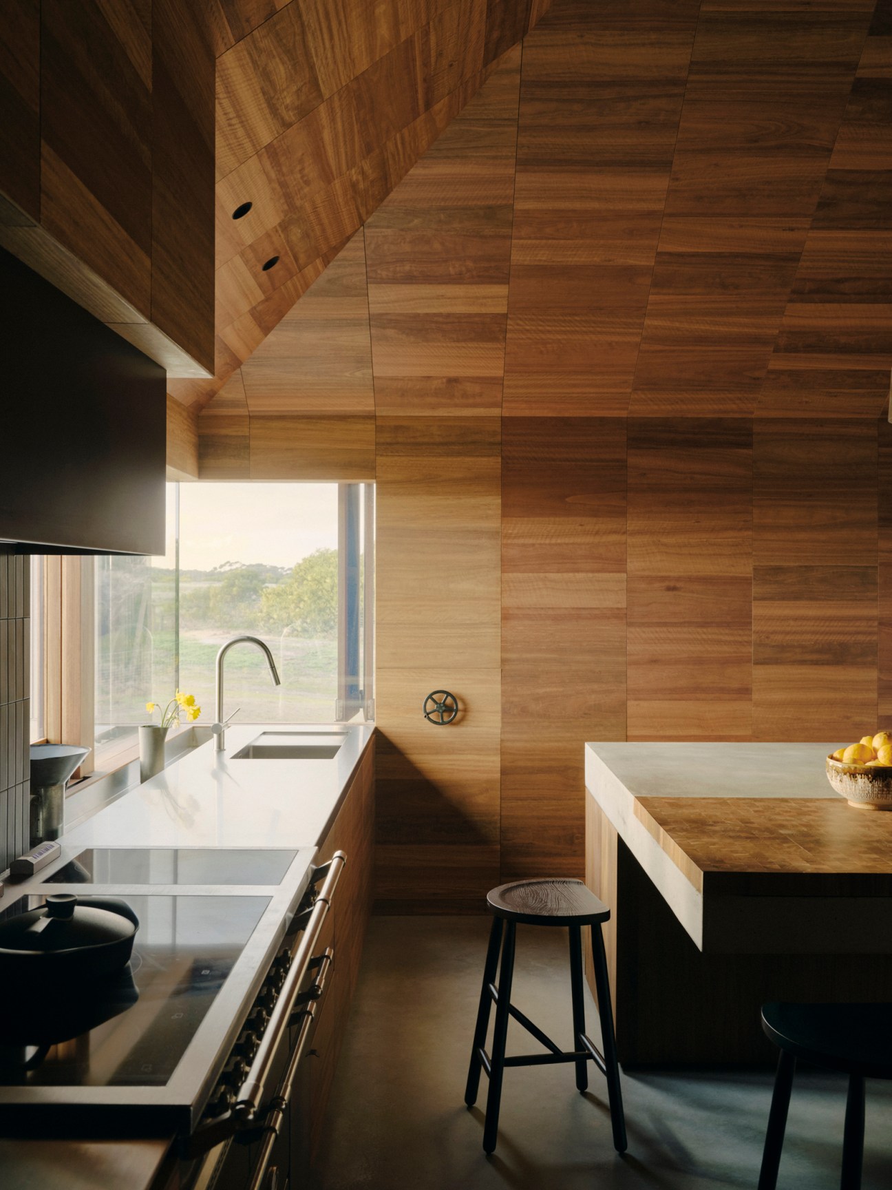 Modern kitchen with wood-paneled walls, white countertops, undermount sink, and bar stool