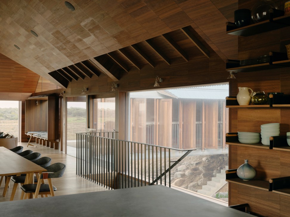 Interior view of farmhouse showing timber-lined ceiling, dining area, metal stair railings and courtyard beyond