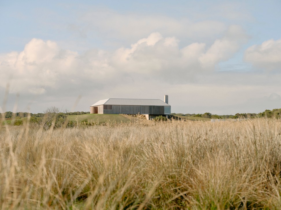 Modern farmhouse with corrugated metal roof set in golden grassland under cloudy sky