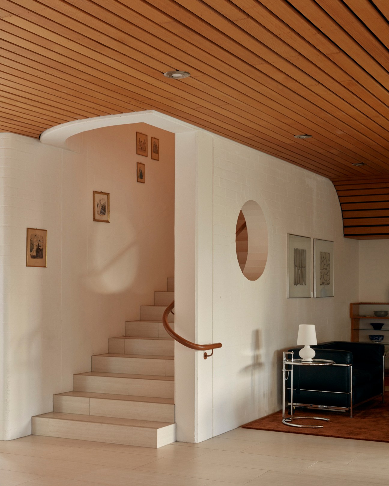 Interior view showing curved staircase with white walls, wooden handrail, and wood slat ceiling