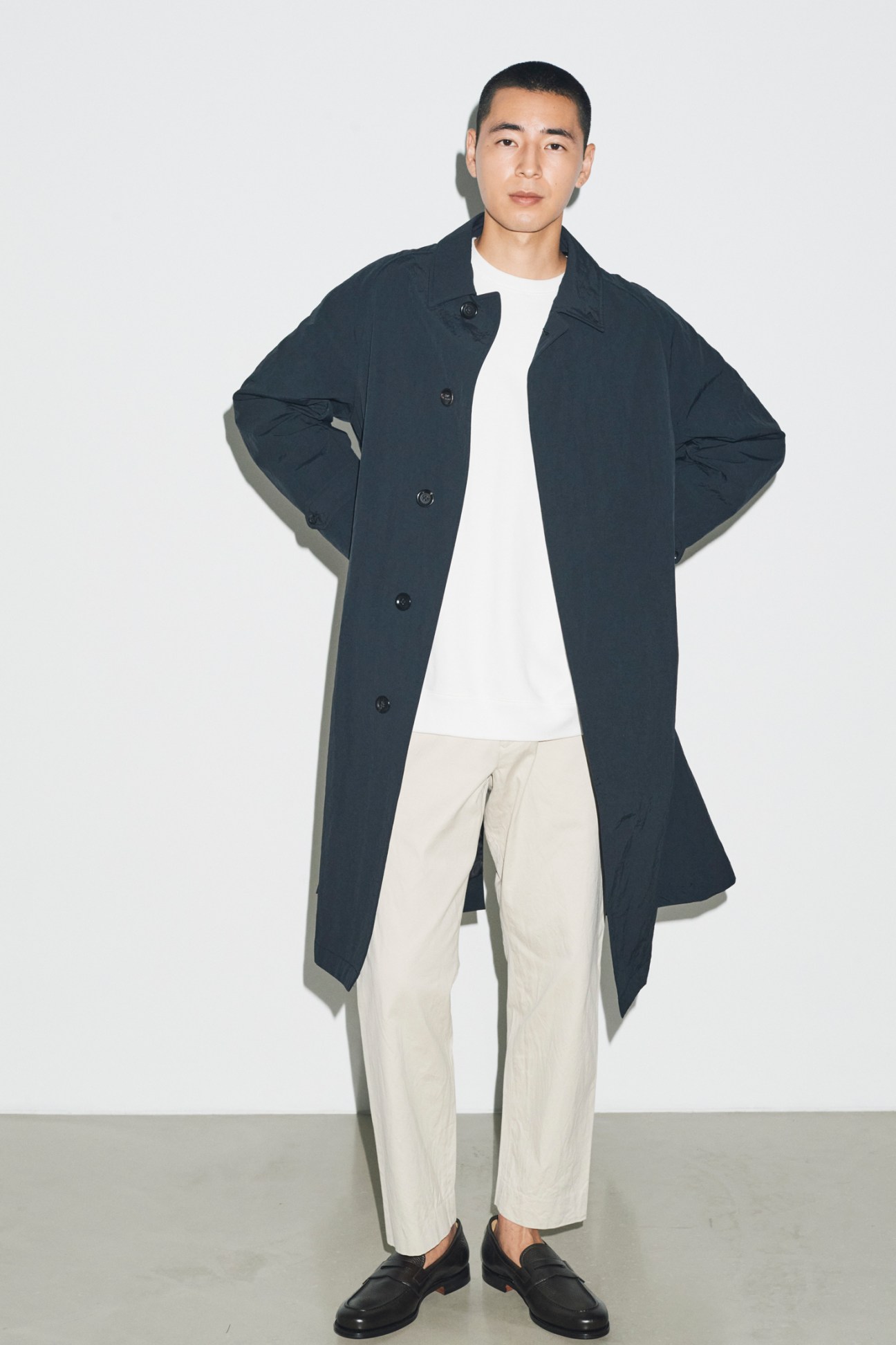 Model in casual autumn layering with dark coat over white sweatshirt and beige trousers, wearing leather shoes