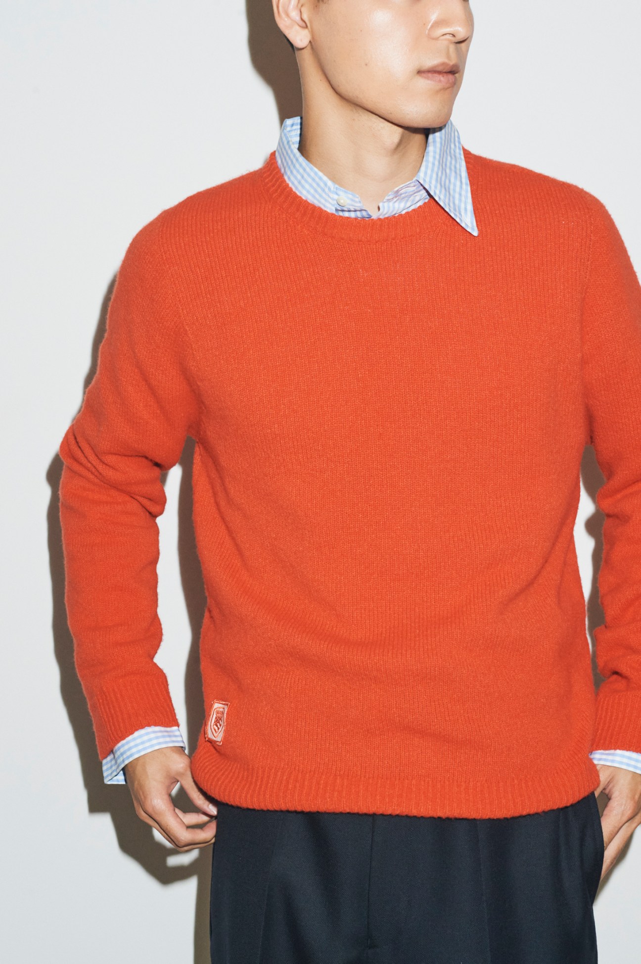 Model wearing red jumper over striped shirt with dark trousers in autumn layering style