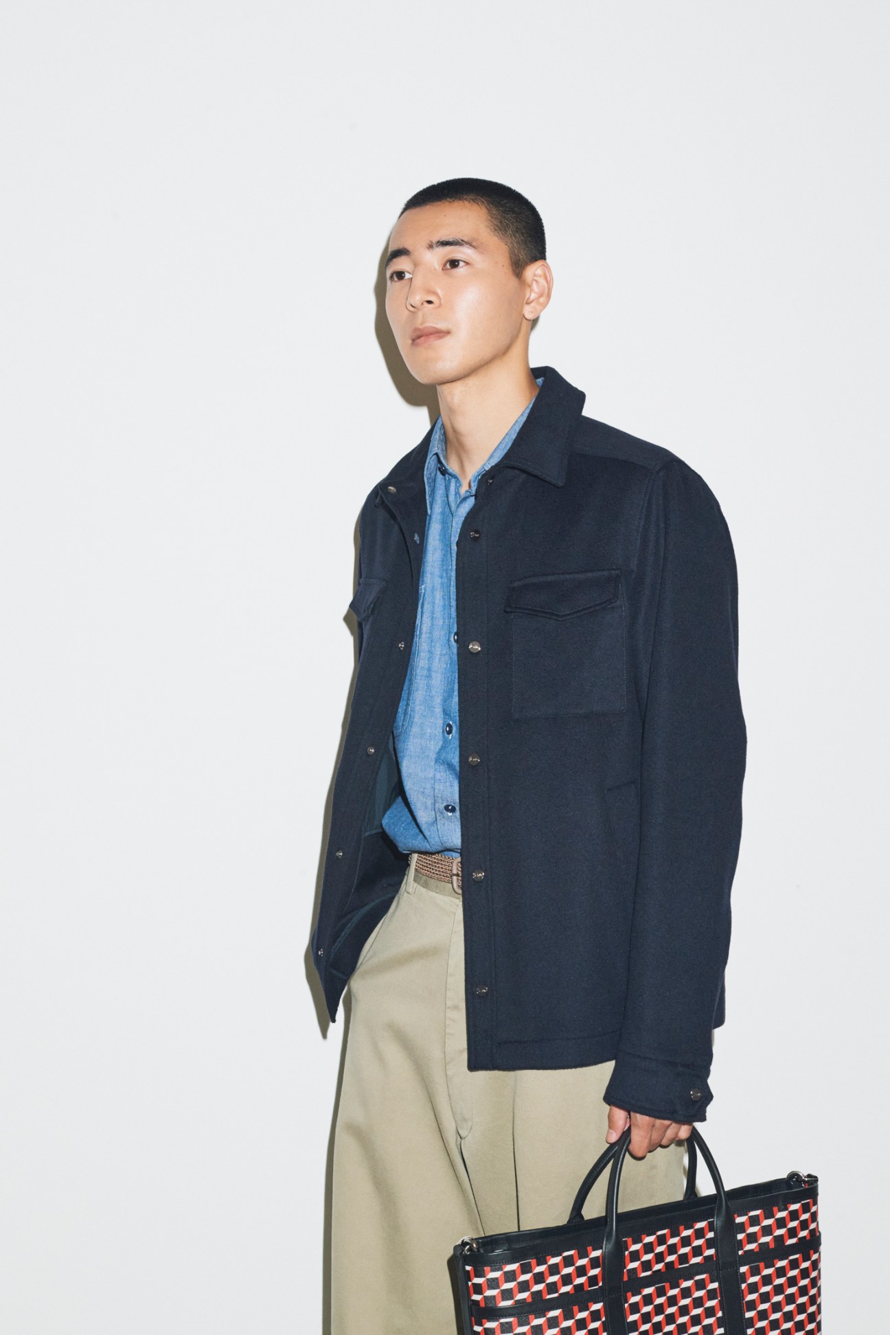 Model wearing navy jacket over blue shirt with beige trousers and patterned bag