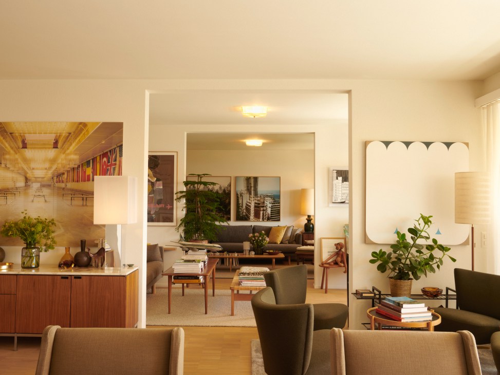 Open-plan living space with mid-century furniture, built-in shelving, and large windows overlooking a lake