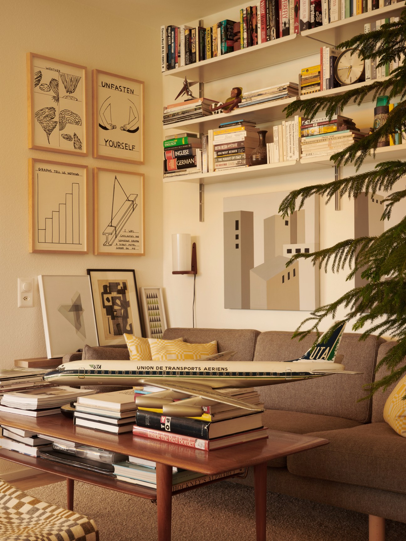 Living room with wooden coffee table, books, vintage airplane model, framed wall art, gray sofa and plant