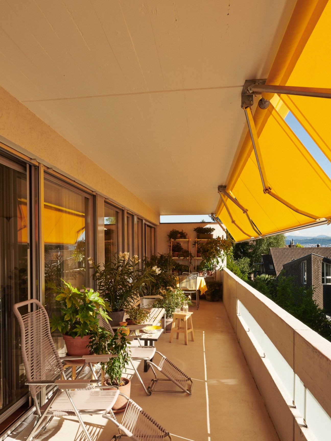 Outdoor balcony with yellow awning, wicker chairs, potted plants and view of residential buildings