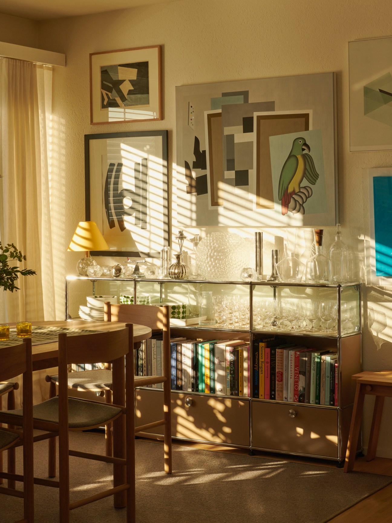 White modular shelving system next to wooden dining table with artwork on walls