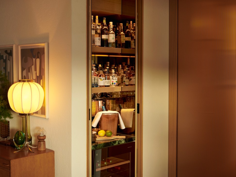 Built-in bar with open wood doors revealing liquor bottles on shelves and V-Zug wine fridge below