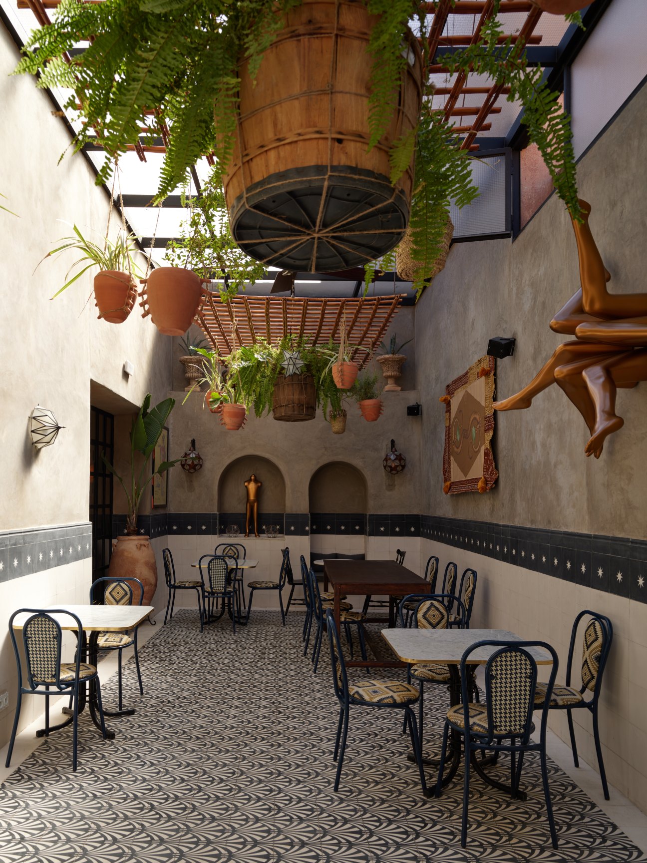 Indoor courtyard dining area with geometric patterned floor, bistro tables and chairs, hanging plants and pergola