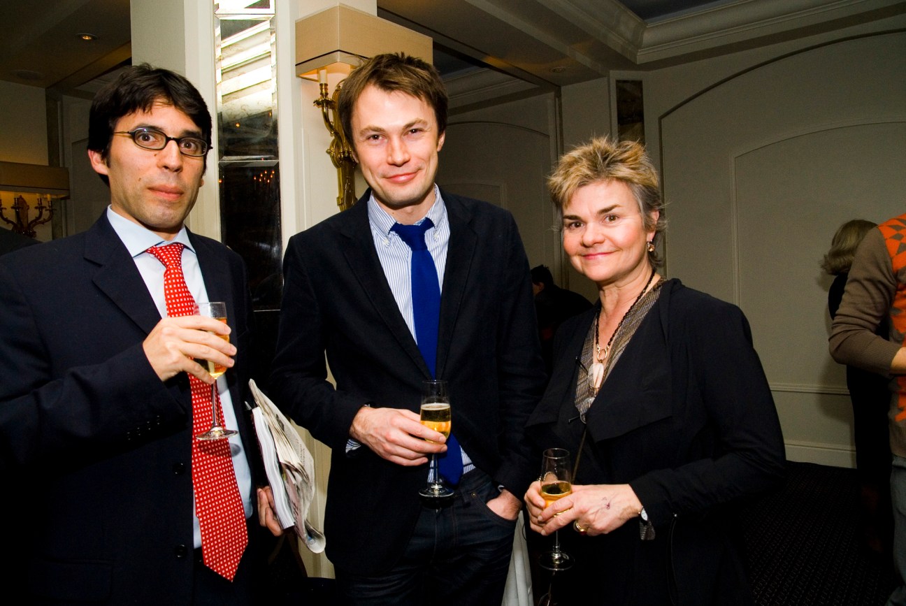 Three people in business attire holding drinks at an indoor event