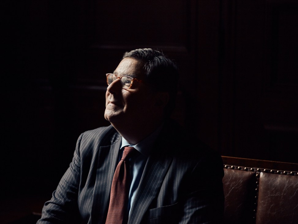 Man in pinstriped suit and red tie wearing glasses, photographed in profile against dark background.