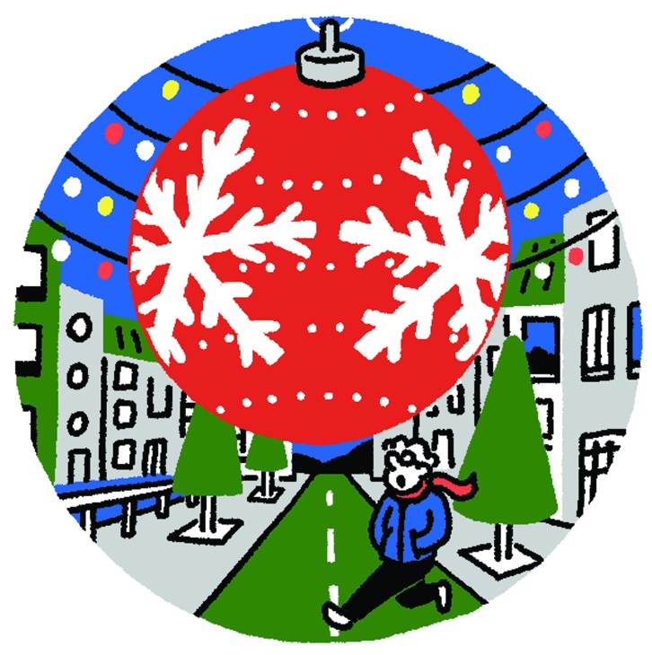 Person in winter clothing looking up at large red Christmas ornament with snowflakes above snowy street with buildings and evergreen trees