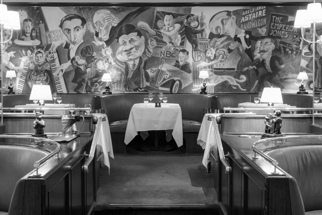 Interior of Monkey Bar restaurant showing banquette seating, table lamps, and colorful mural wall