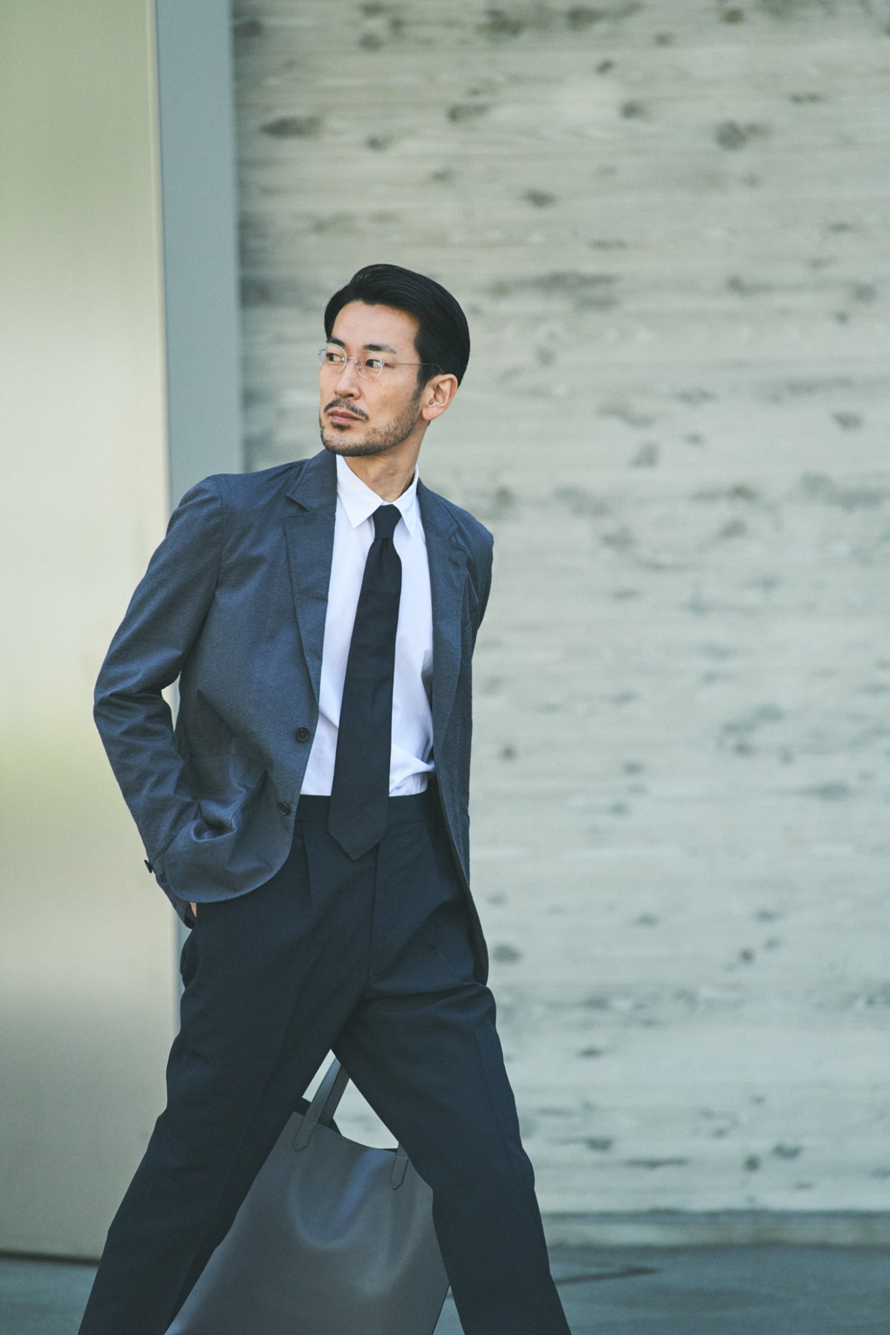 Man in navy suit and tie walking against concrete wall backdrop in Tokyo