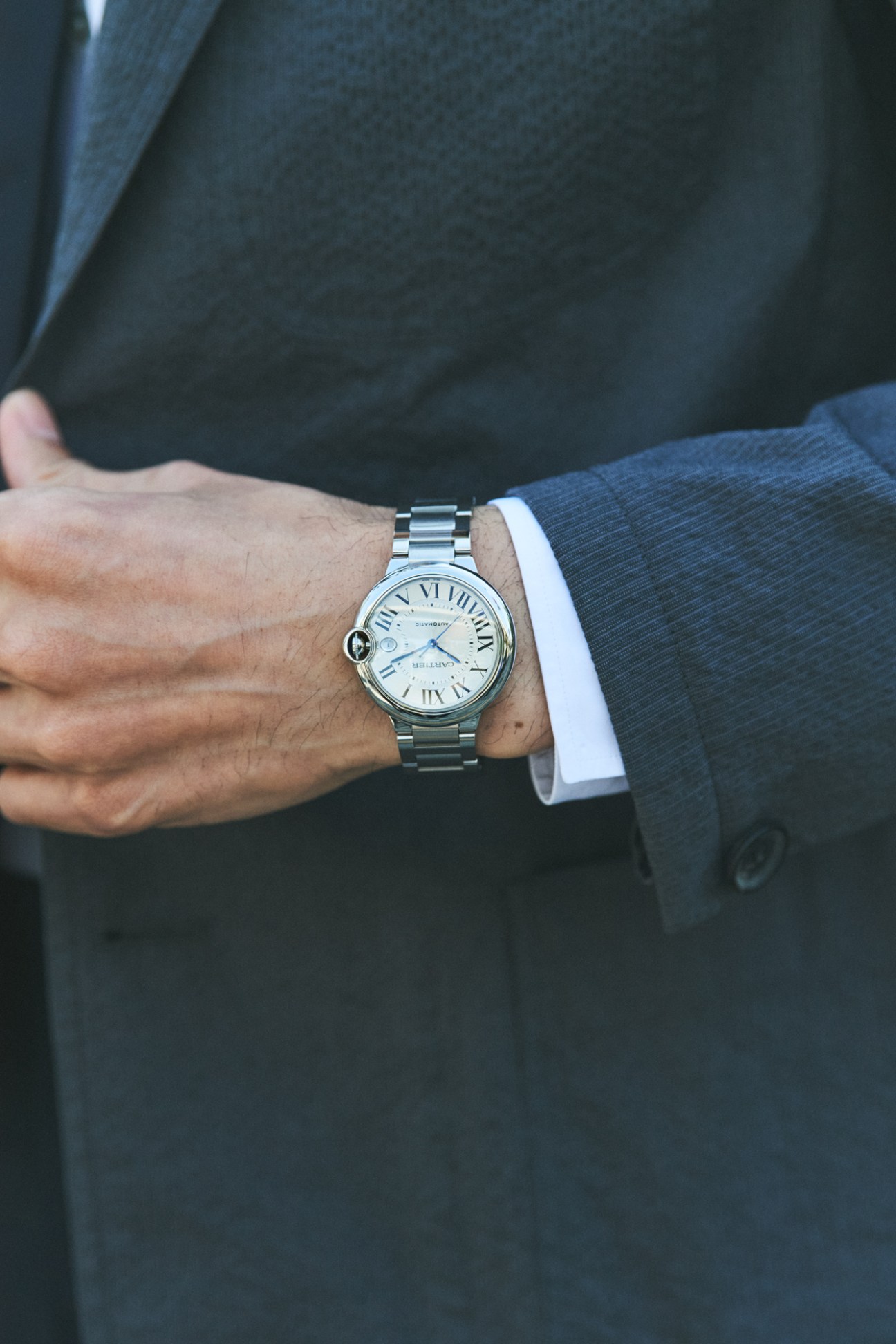 Close-up of man's wrist wearing Cartier watch with Roman numerals and steel bracelet in business attire