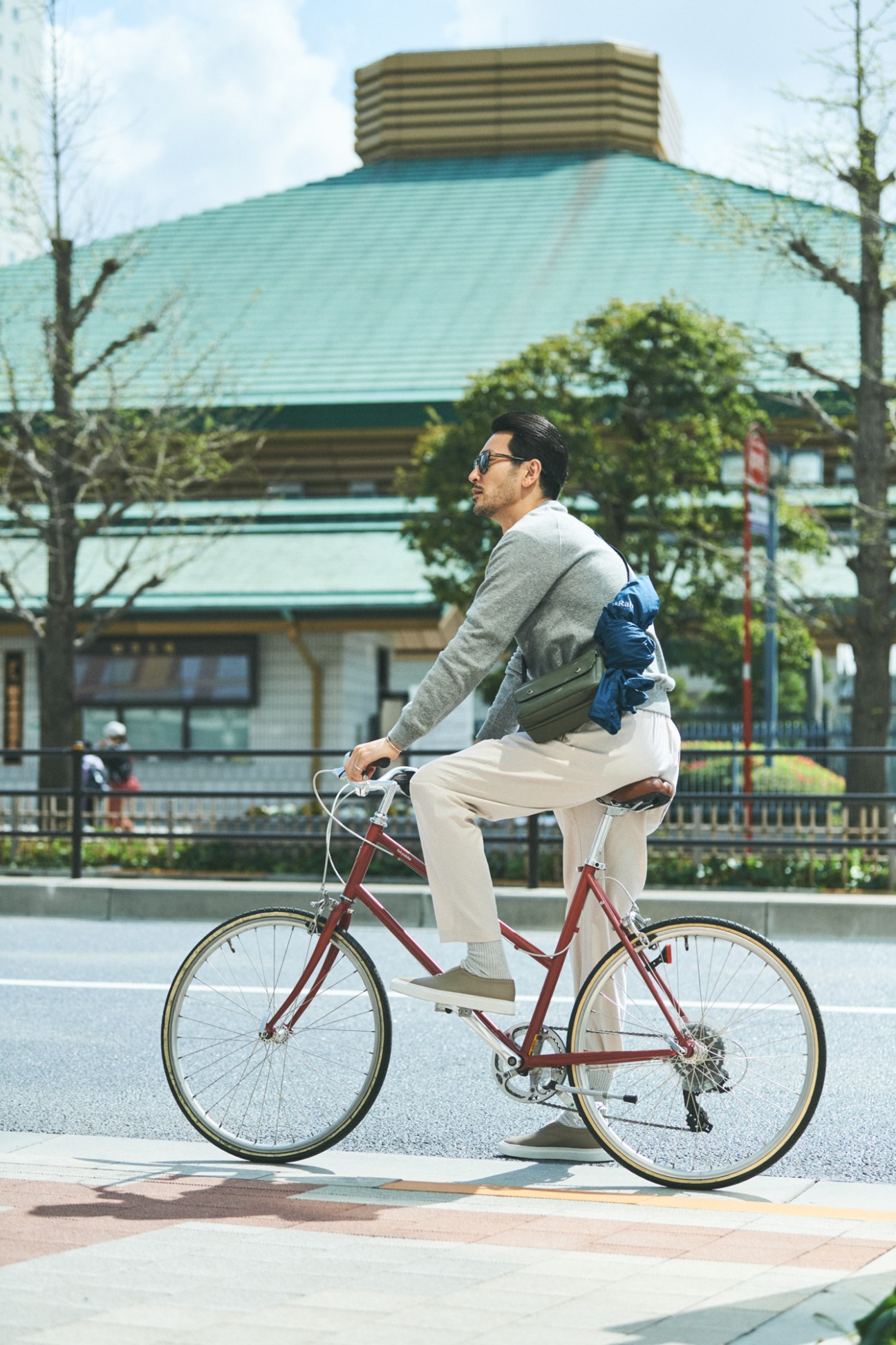 Man on red bicycle wearing grey sweater and beige trousers in Tokyo street