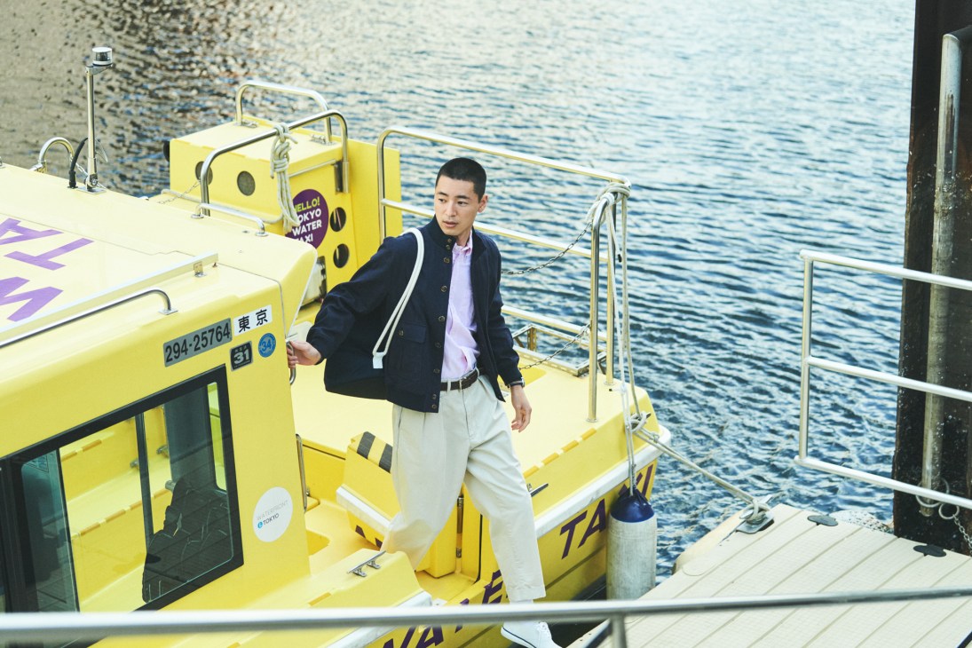Man in dark jacket and light trousers standing on yellow water taxi at Tokyo dock