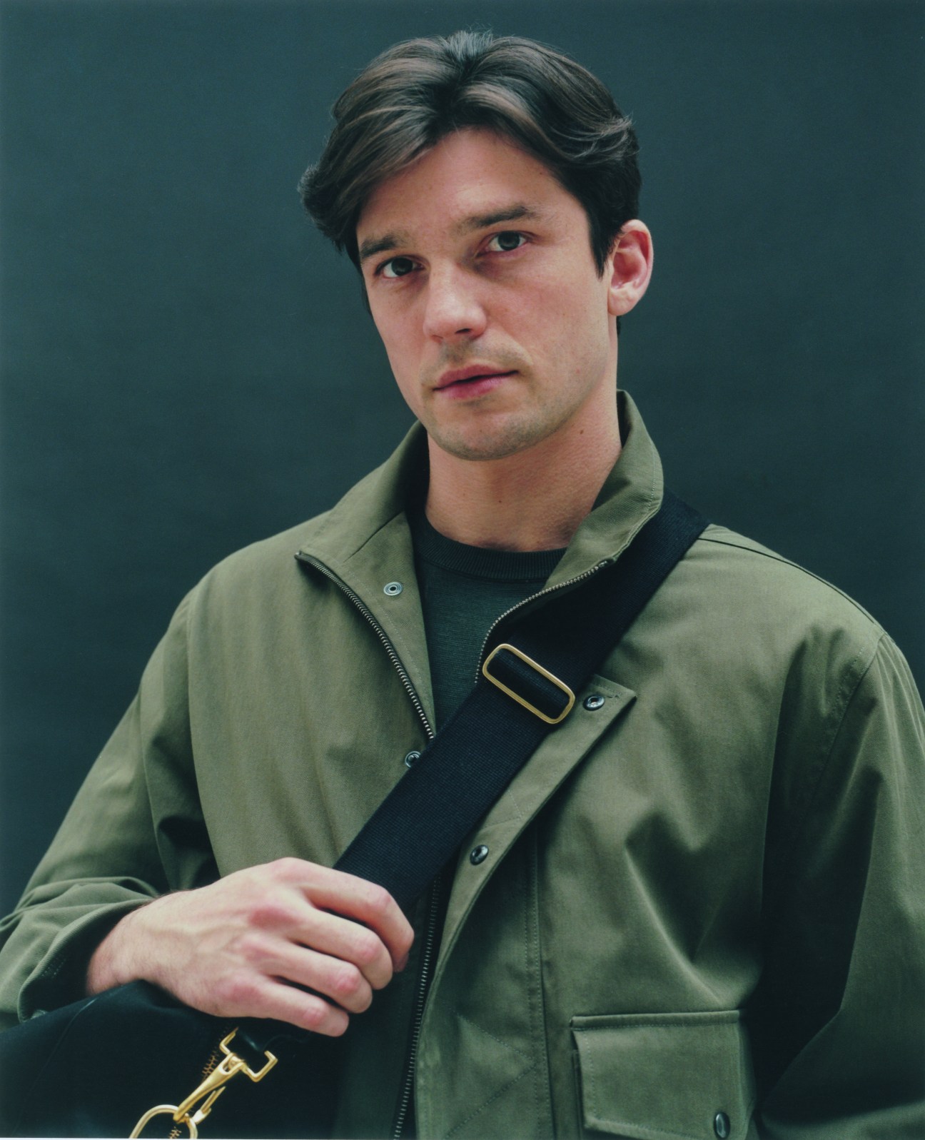 Man in olive green Margaret Howell jacket and black t-shirt with black Brady crossbody bag