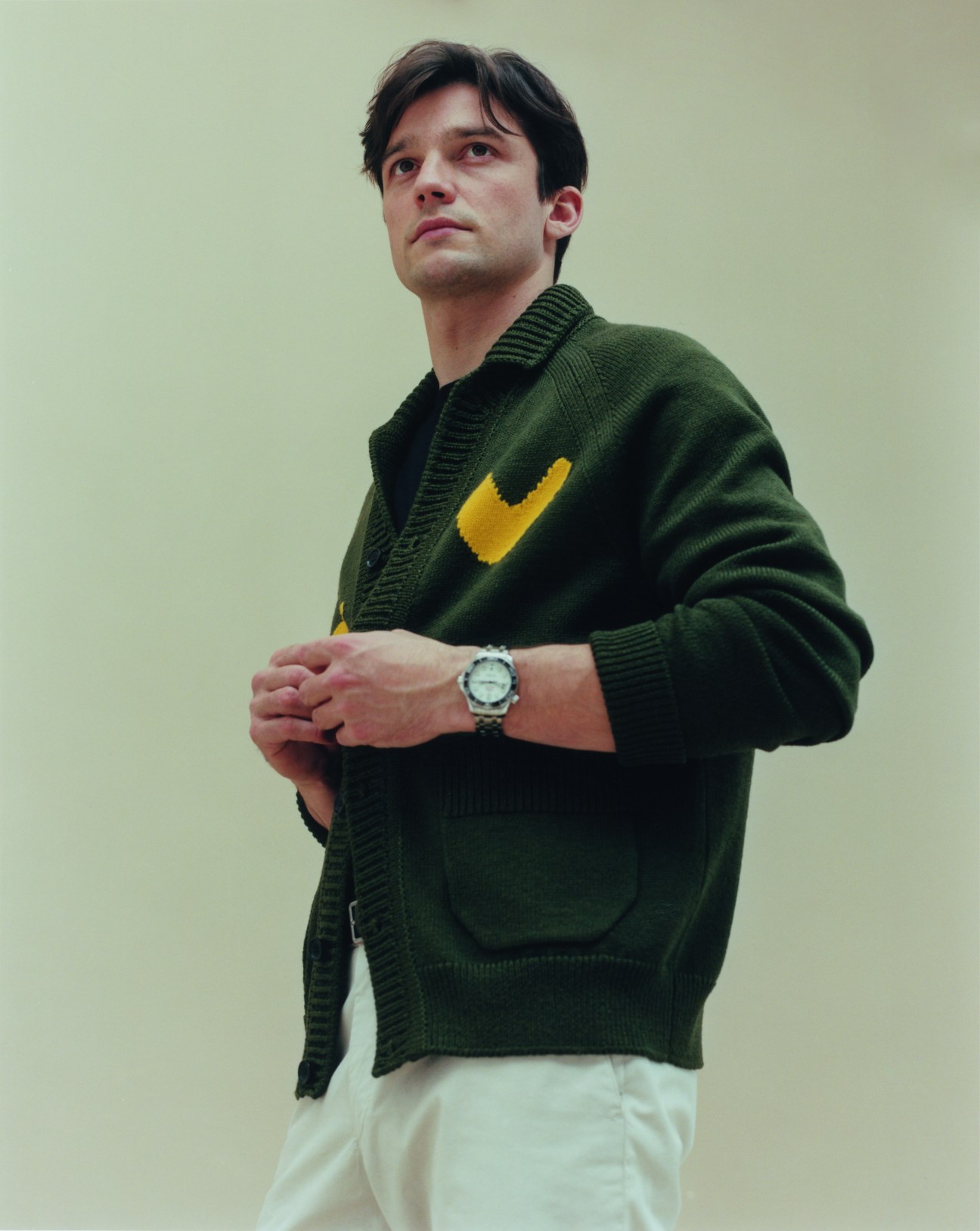 Man in green Louis Vuitton cardigan with yellow detail and white trousers looking upward